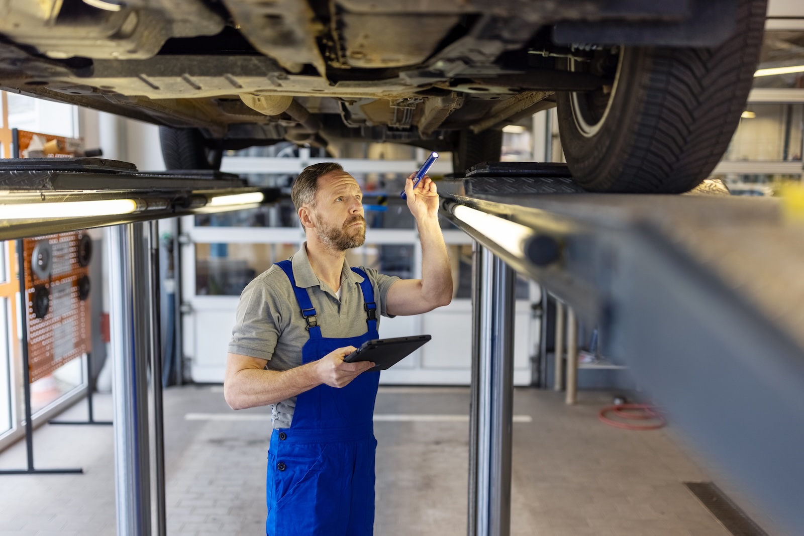 Mechanik z latarką sprawdza podwozie podniesionego samochodu podczas przeglądu technicznego.