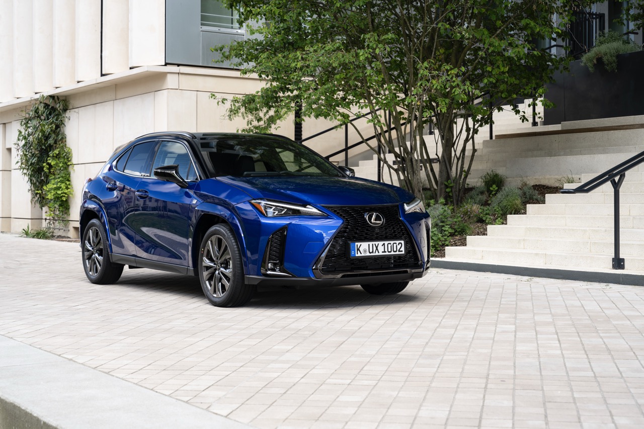 Niebieski Lexus UX zaparkowany na podjeździe przed nowoczesnym budynkiem.