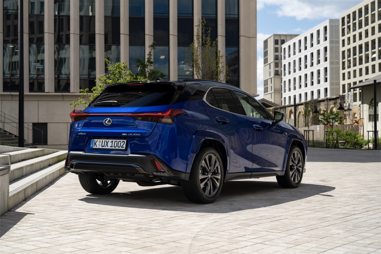 Niebieski Lexus UX 300h zaparkowany na placu przed nowoczesnymi budynkami.
