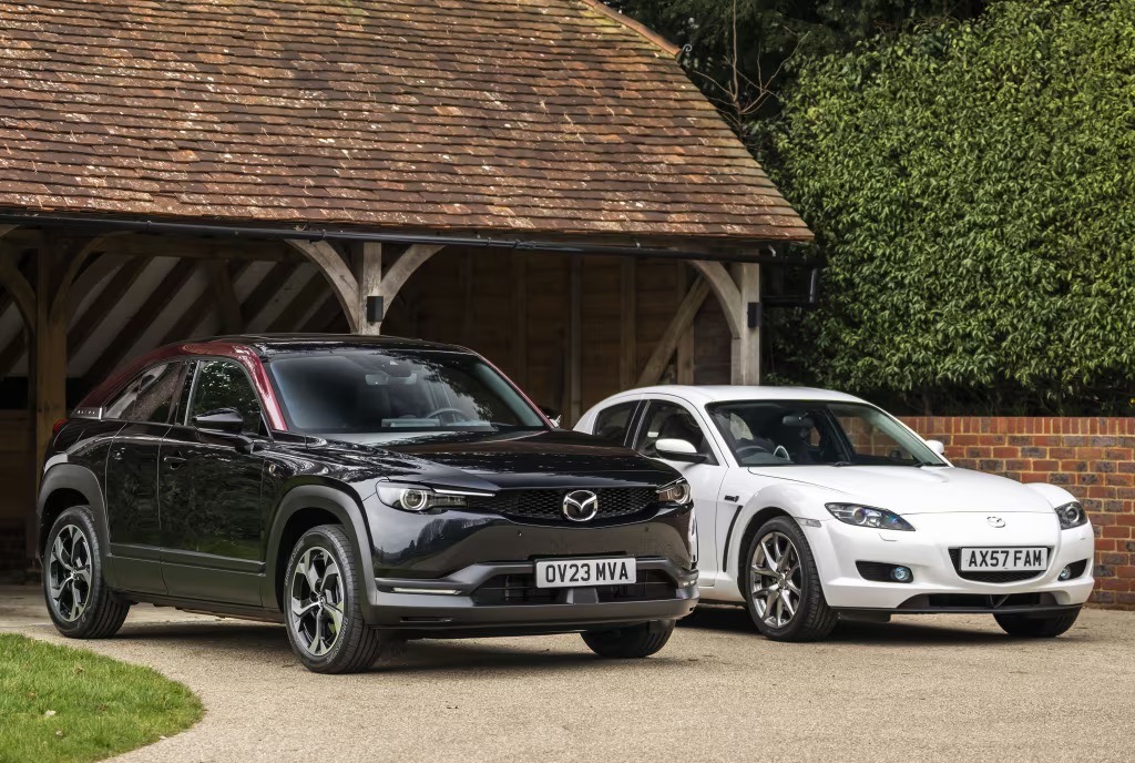 Czarna Mazda MX-30 i biała RX-8 stoją obok siebie pod drewnianą werandą.