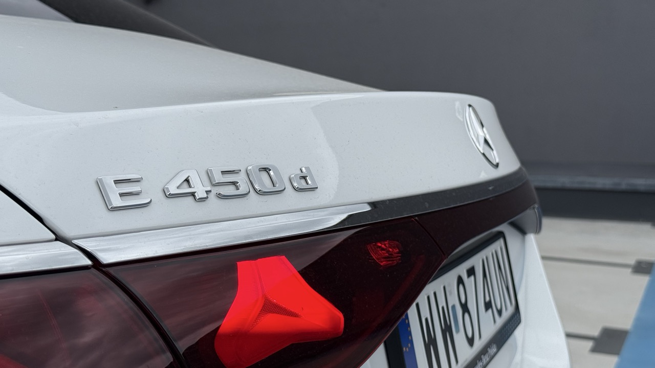 Srebrny napis E 450d na tylnej klapie białego mercedesa.