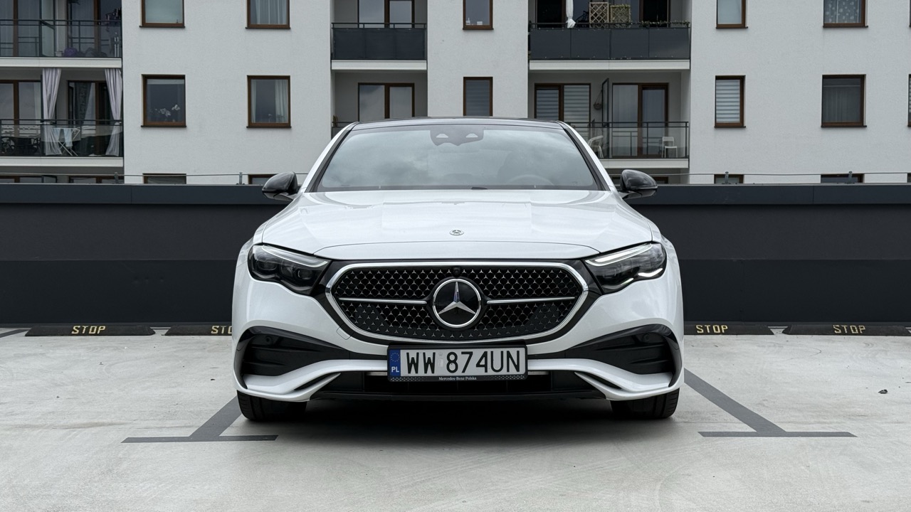 Biały Mercedes-Benz zaparkowany na miejscu parkingowym przed budynkiem mieszkalnym.