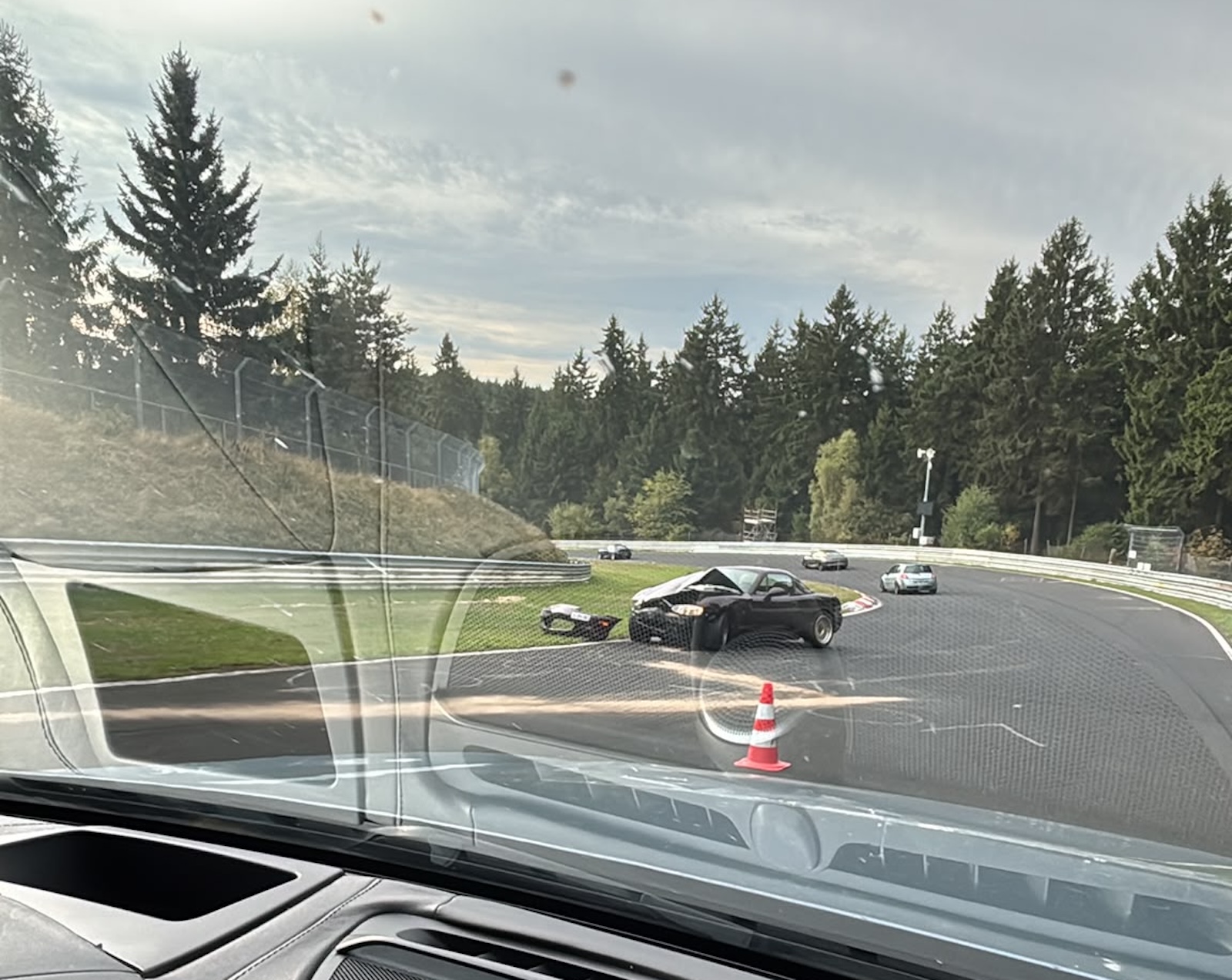 Czarny samochód sportowy z uszkodzoną maską na zakręcie toru Nürburgring, tuż obok pachołka.