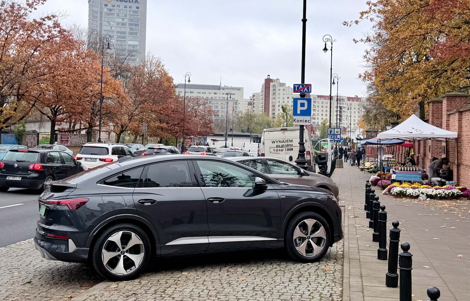 Ciemnoszary SUV zaparkowany na miejskiej ulicy, z miejscem parkingowym przy cmentarzu.