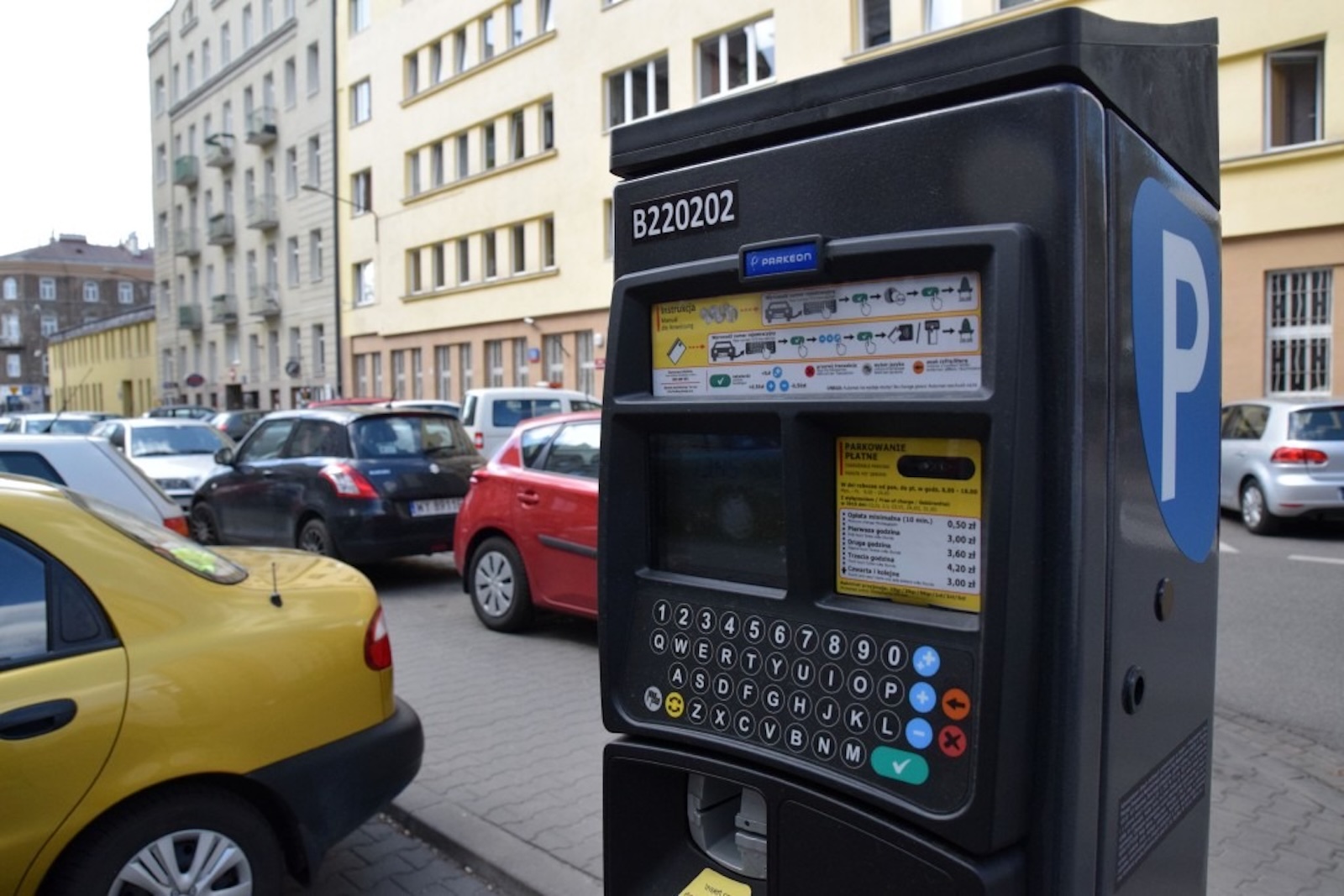 Parkometr z klawiaturą i instrukcją płatności przy ścieżce dla dzieci z kartą rowerową.